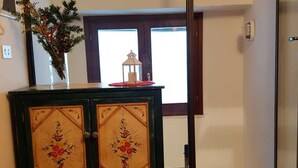 A room with a wooden floor, a blue mat, a cabinet with floral designs, a plant, and a window with a view. - Attic in the center of Assisi (Assisi)