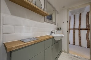 Une salle de bain avec un plan de toilette en bois, un lavabo et un miroir. Une porte avec un cadre en bois donne accès à une autre pièce.