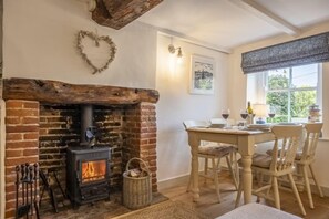 Une pièce chaleureuse avec une cheminée en briques, une table à manger avec des chaises et une fenêtre donnant sur un paysage verdoyant.