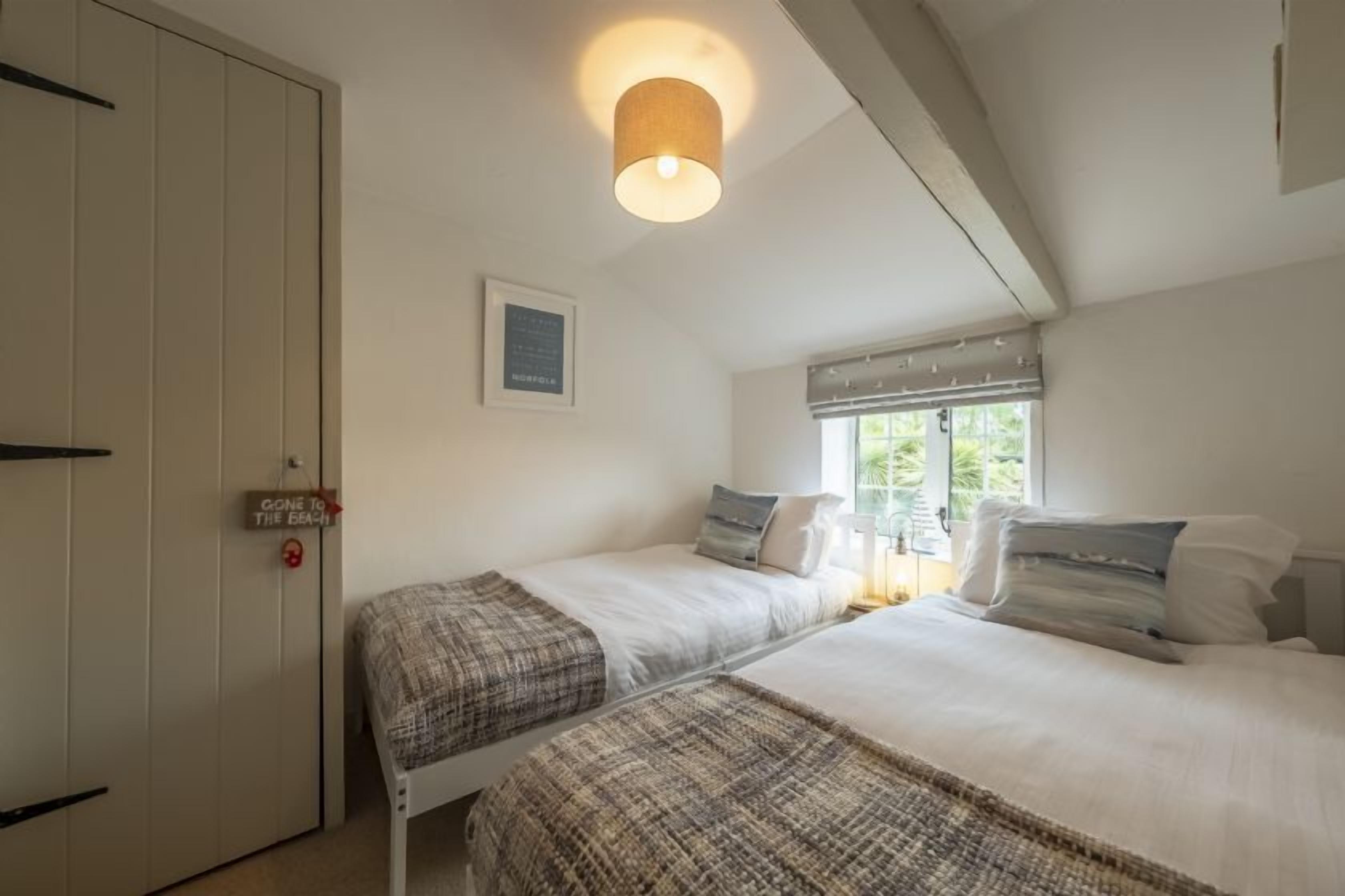 Ein Schlafzimmer mit zwei Betten, einem Fenster mit Jalousien, einer Tür mit einem Schild und einer Deckenleuchte.