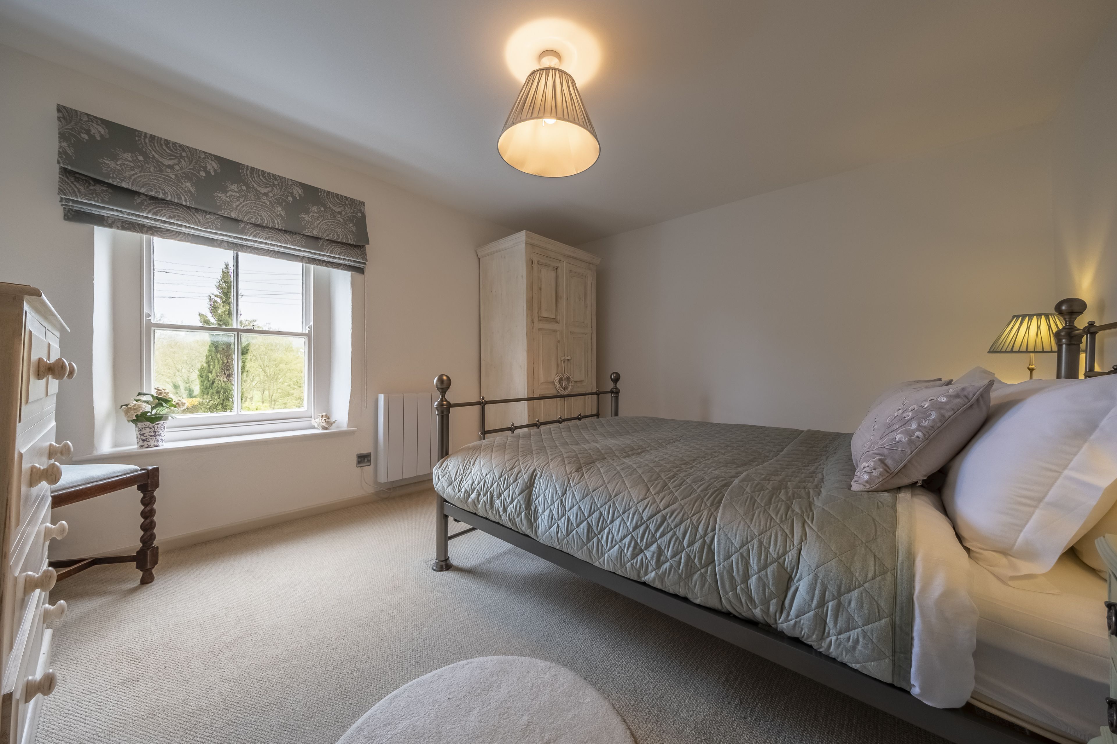A bedroom with a bed, a window with a view, a wardrobe, and a lamp.