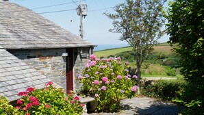 A stone cottage with a red door, surrounded by lush greenery and pink flowers. - Spacious Cottage With Sea Views (Trevillett)