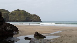 A beach with rocky outcrops and a calm sea. - Spacious Cottage With Sea Views (Trevillett)