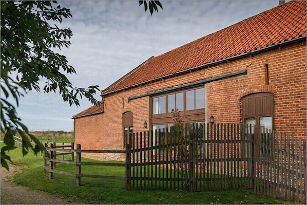 A brick building with a tiled roof, large windows, and a wooden fence.