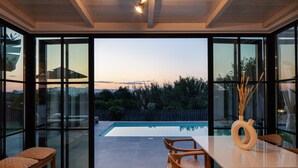 A modern dining area with a pool view, featuring a wooden table and chairs, a bench, and a vase with reeds. - Walking Distance to Platanias Centre and the Beach! Heated pool! (Chania)