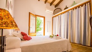 Ein Schlafzimmer mit Bett, Lampe, Fenster mit Vorhängen und Blick auf Grün.