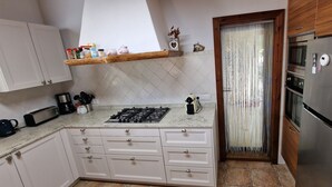 Eine Küche mit weißen Schränken, einem Edelstahlkühlschrank, einem Gasherd und einem Holzregal mit Küchenutensilien.