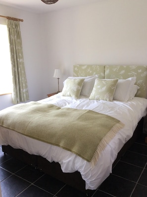 A neatly made bed with a green patterned headboard and matching pillows, a white throw blanket, and a floor lamp beside the bed.
