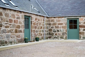 A stone building with two green doors and a gravel courtyard.