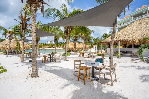 Un resort frente a la playa con sombrillas de techo de paja, palmeras y zonas de estar al aire libre.