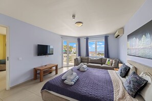A hotel room with a bed, a sofa, a television, and a painting.