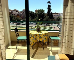Un balcon avec une table et des chaises, un pot de fleurs et une vue sur une rue et des immeubles.