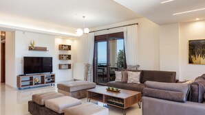 Un salon moderne doté d’un téléviseur à écran plat, de sièges confortables, d’une table basse et d’une grande fenêtre agrémentée de rideaux.