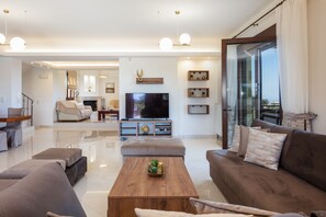 A modern living room with a flat-screen TV, a wooden coffee table, and a brown sofa. - Rosemary Villa, 45m2 pool, large terrace, walking distance to shops (Rethymno)