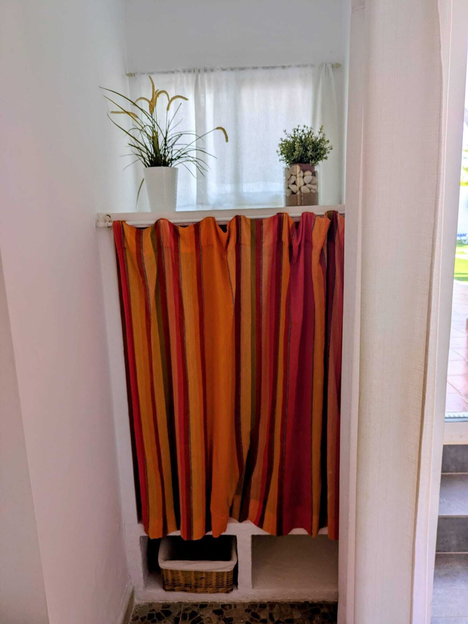 A bathroom with a striped shower curtain, a small potted plant, and a wicker basket.