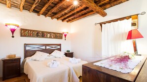Une chambre avec deux lits, des poutres apparentes en bois au plafond, des lampes fixées au mur et une table de chevet avec une lampe.