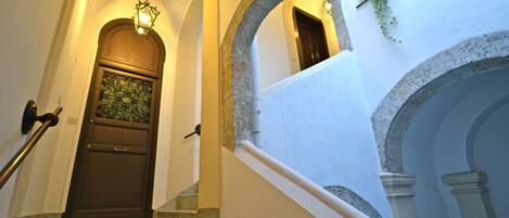 Una escalera con una puerta de madera oscura, un accesorio de iluminación arriba y vista a un área exterior mediante un arco.
