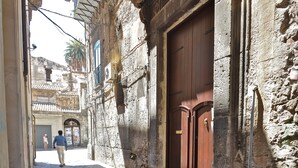 A narrow cobblestone street with a large wooden door and a satellite dish on the building.