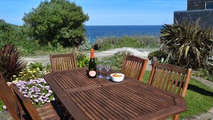A wooden table set outdoors with a bottle and glasses, overlooking a coastal view.