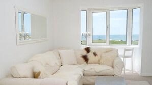 A white living room with a large window, a white sofa, a small table, and a chandelier.