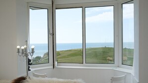 A room with a large bay window offering a view of a grassy landscape and the sea.
