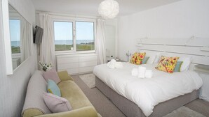 A bedroom with a large bed, a sofa, a TV, and a view of the sea.