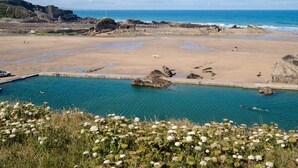 A coastal beach with a clear blue sky, rocky terrain, and a swimming pool.