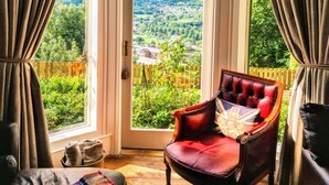 Ein Zimmer mit großem Fenster, einem roten Sessel, Holzboden und einer karierten Decke.