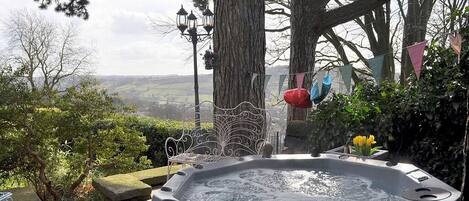 A hot tub with a wrought iron chair, surrounded by greenery and a scenic view.