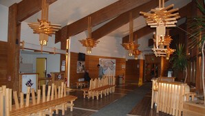 Un amplio vestíbulo con bancos y mesas de madera, vigas altas de madera y lámparas colgantes de madera.