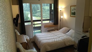 Un dormitorio con cama, escritorio, silla, lámpara y ventana con vista a un bosque.