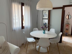 Un coin repas avec une table ronde, des chaises blanches et un vase rempli de fleurs.