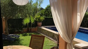 Eine Außenpatio mit rundem Tisch und Stühlen, einer hängenden Leuchte, einem Pool und Kübelpflanzen.