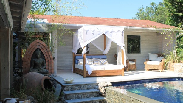 Eine Holzjagdhaus mit Bett unter einem Baldachin, einer Meditationsstatue und einem Swimmingpool.