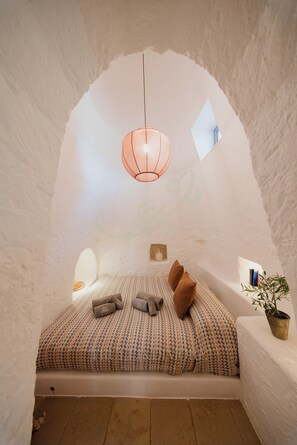A cozy room with a bed, pillows, a hanging light fixture, and a small window.