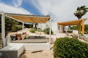 Un área de estar al aire libre cubierta con un sofá blanco, una pérgola y una piscina.