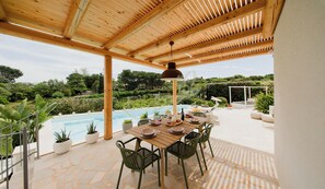 An outdoor dining area with a pool, wooden pergola, and potted plants.