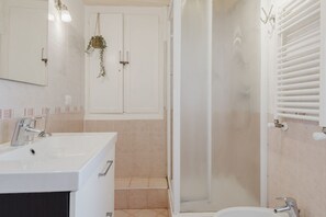 Un baño con lavamanos blanco, espejo y cabina de ducha.