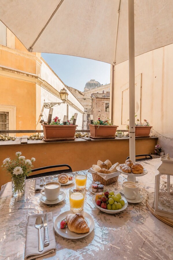A table set for breakfast with croissants, fruit, and coffee, overlooking a cityscape with buildings and a dome.
