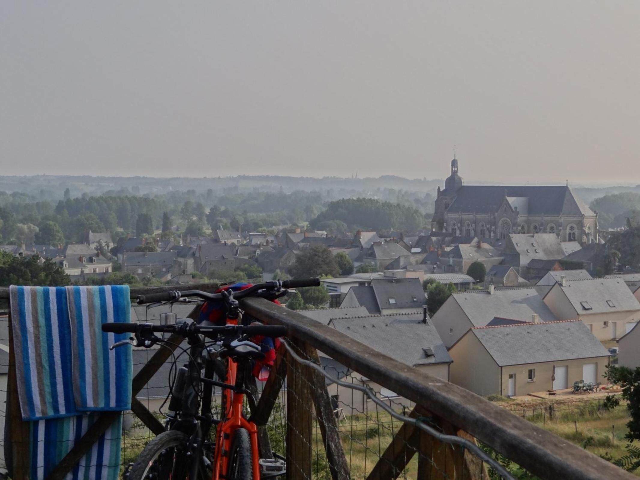 A bicycle leaning against a wooden fence overlooking a town with a prominent church in the background.