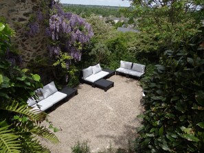 A patio with outdoor seating, surrounded by lush greenery and a stone wall. - Le Moulin Géant (Rochefort-sur-Loire)