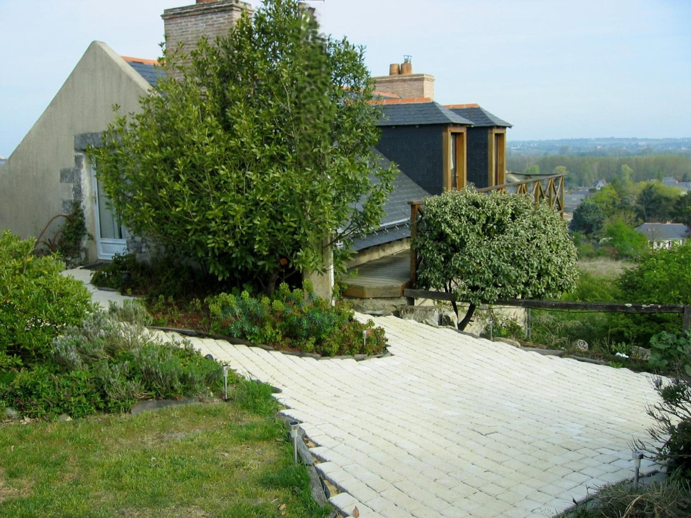 A house with a sloped roof, a wooden deck, and a garden with various plants and trees.
