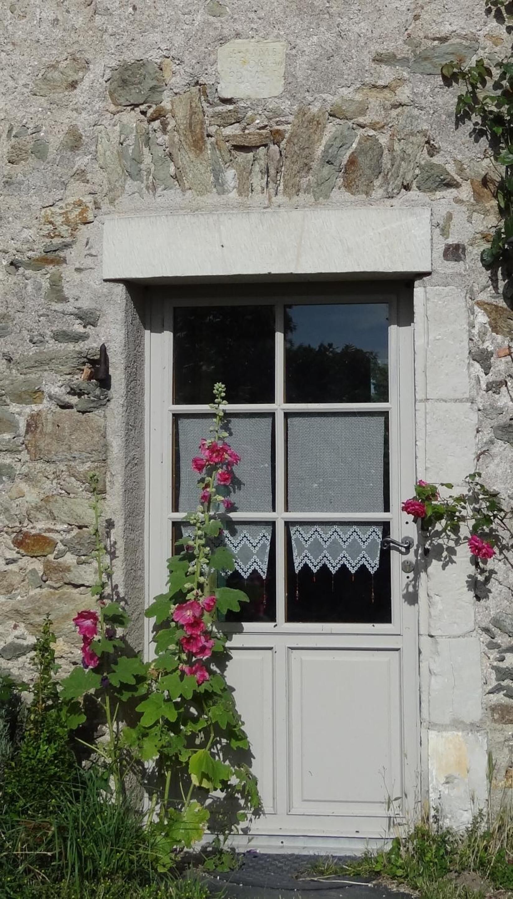 Ein Steinhäuschen mit einem Fenster, verziert mit Spitze und rosa Blumen.