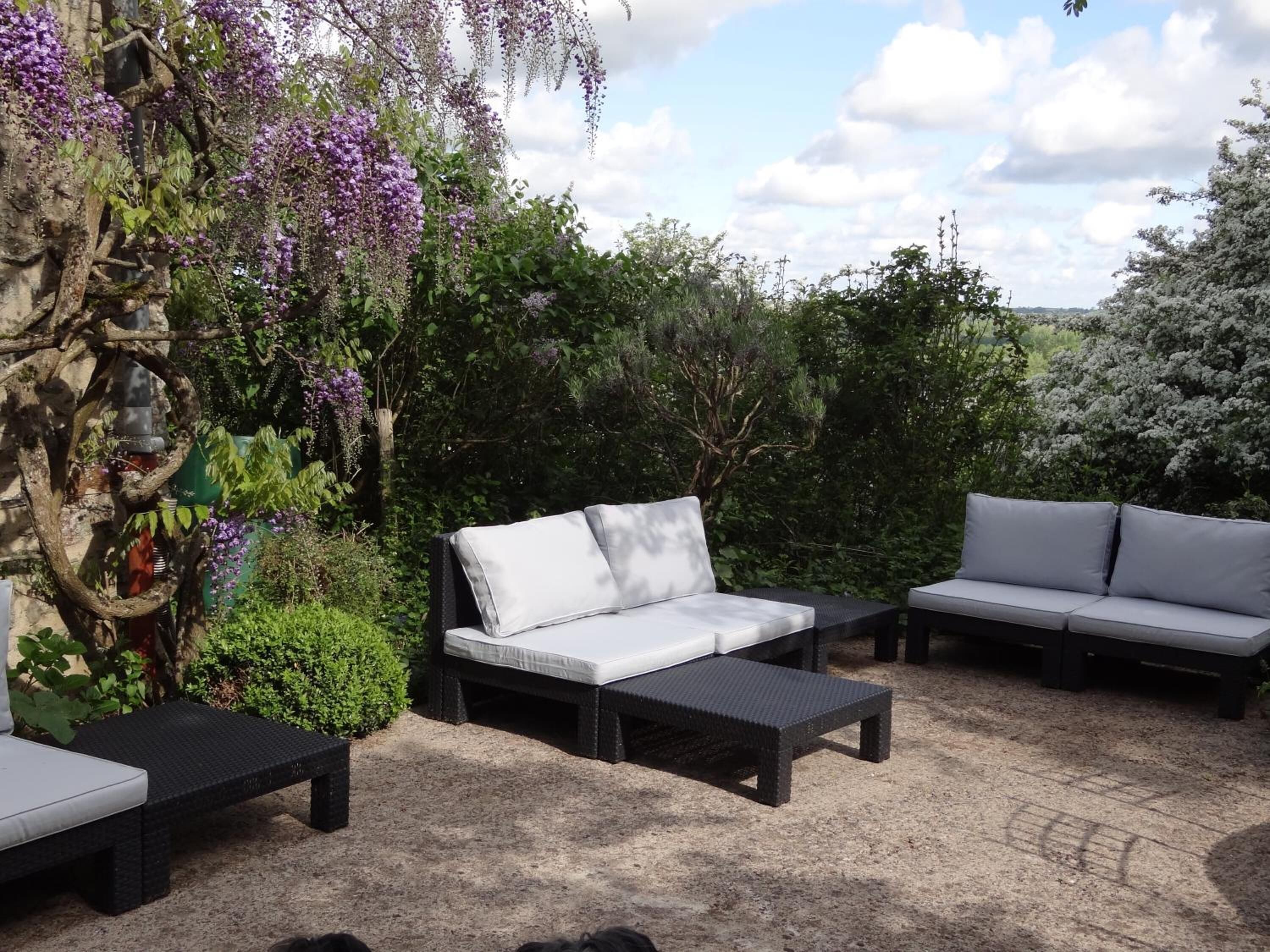 An outdoor seating area with three black wicker sofas and matching cushions, surrounded by lush greenery and flowering plants.