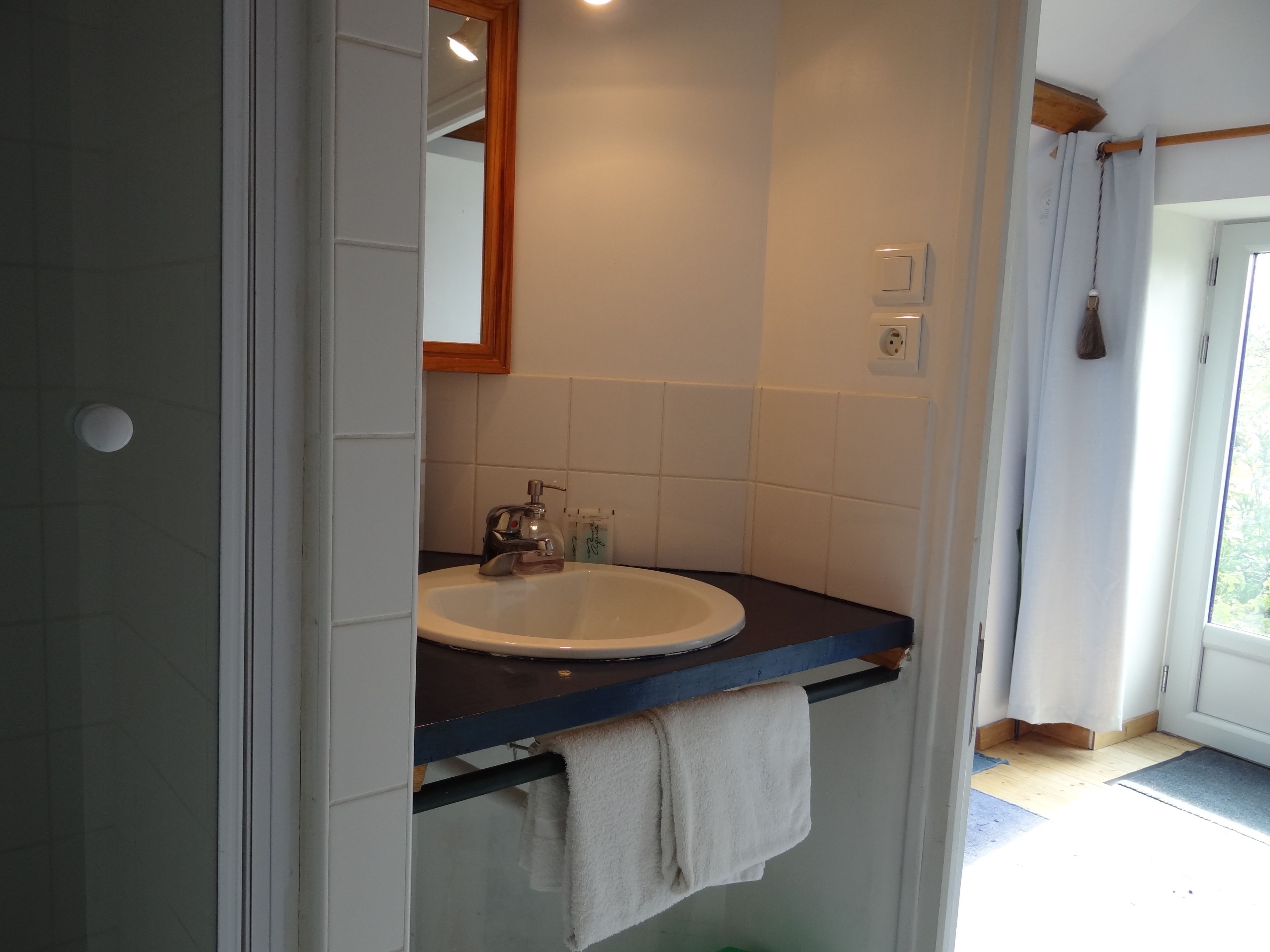 Un baño con un lavabo blanco, un espejo y una toalla colgada en un perchero.