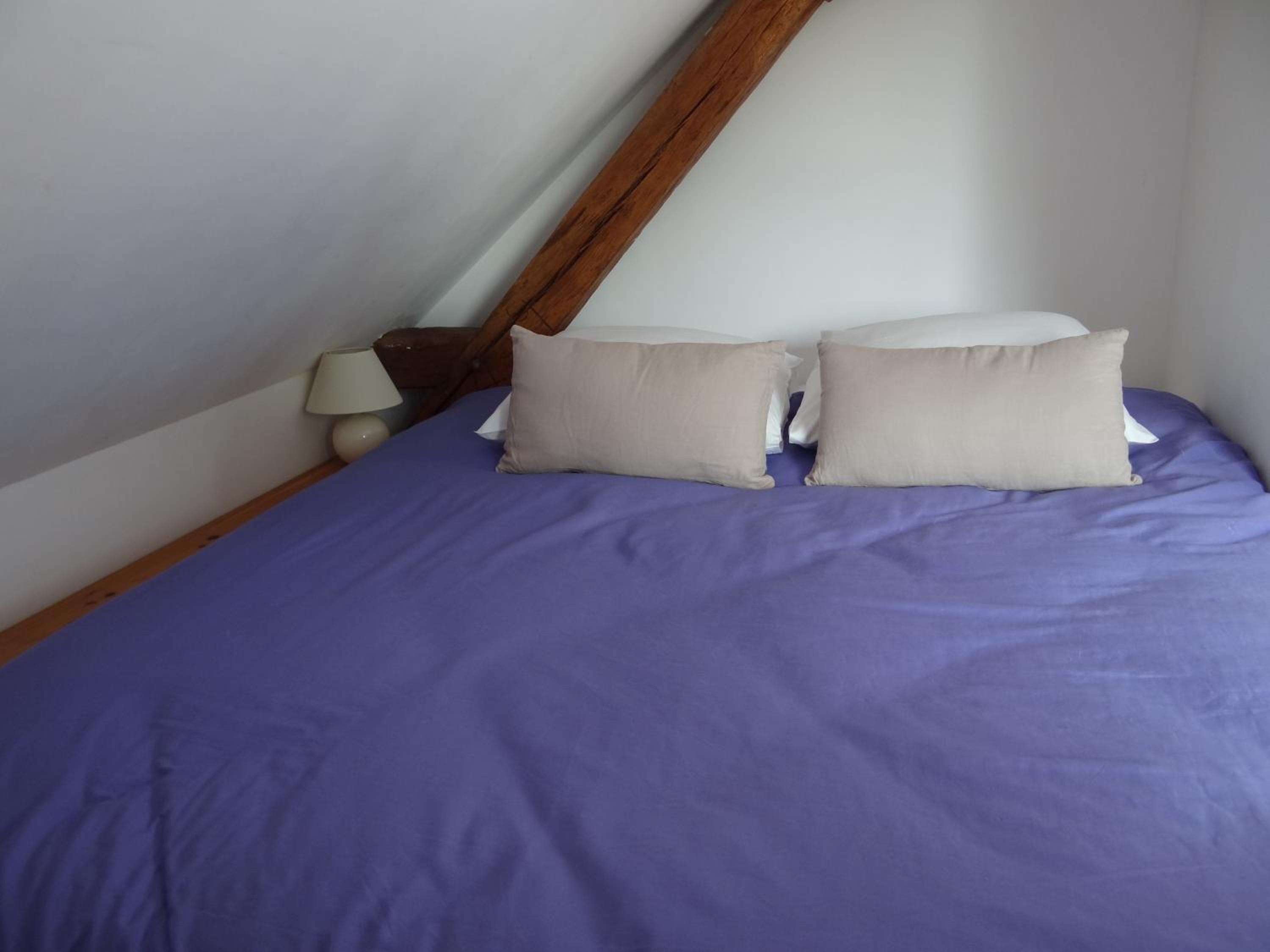 Una cama individual con una colcha morada y dos almohadas color beige.