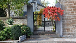 A gated entrance with a stone wall, a metal gate, and a tree with red leaves. - charming country cottage for rent  (Ave et Auffe)