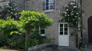 A stone building with a white door, a small balcony, and a garden with flowering plants. - charming country cottage for rent  (Ave et Auffe)