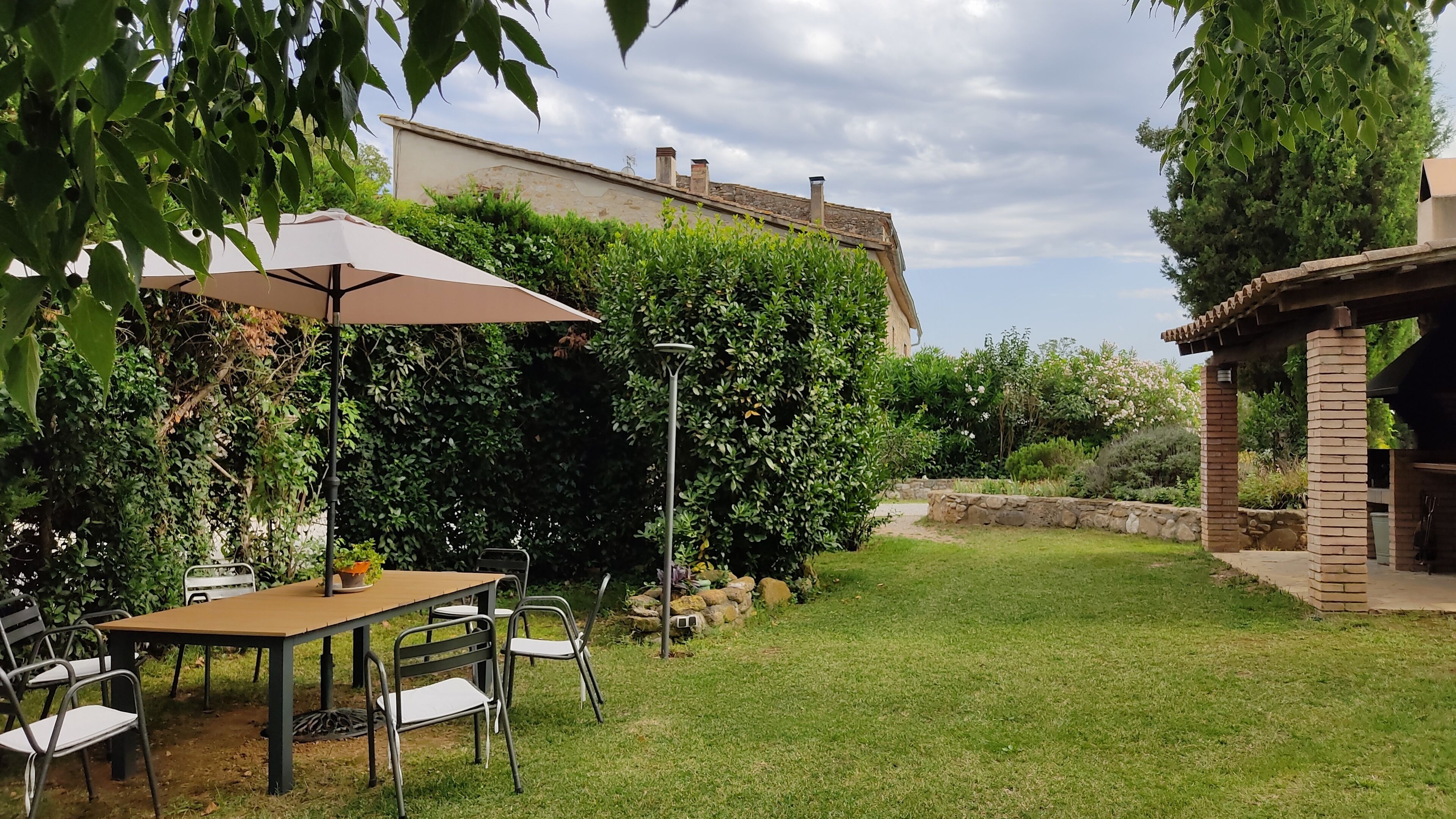 A patio with a table and chairs, surrounded by lush greenery and a stone wall.