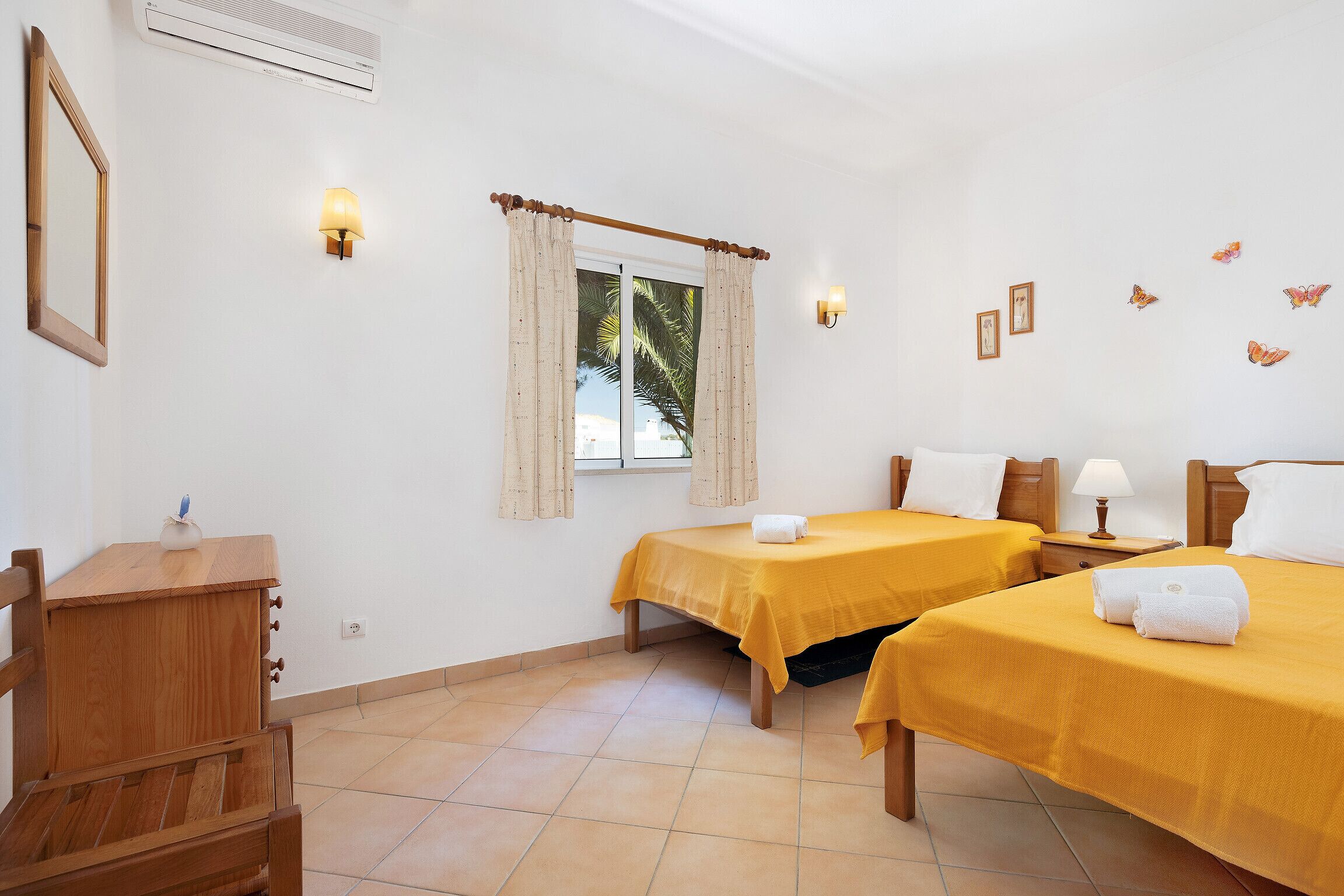 A hotel room with two beds, a wooden dresser, a window with curtains, wall-mounted lights, and butterfly decals.